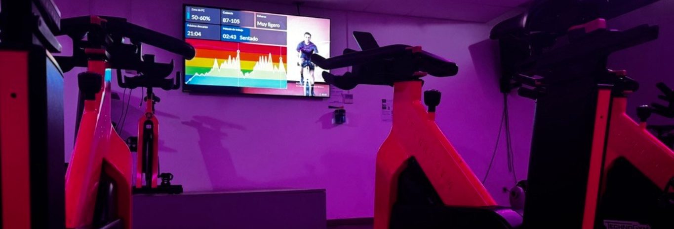 Sala de ciclo indoor a oscuras, con la pantalla de la clase encendida